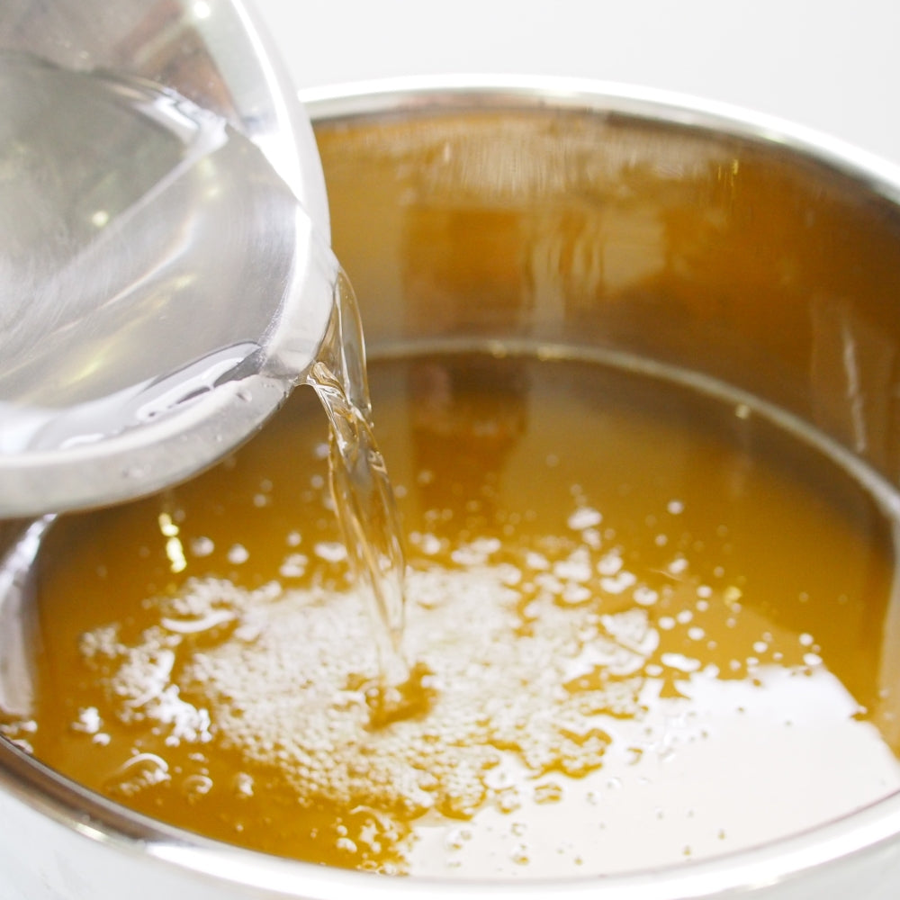 Clear lye solution poured from beaker into steel bowl of oils