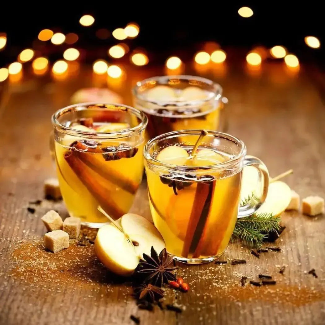 Festive warm apple cider with spices in clear mugs, surrounded by apples and sugar, twinkling holiday lights.