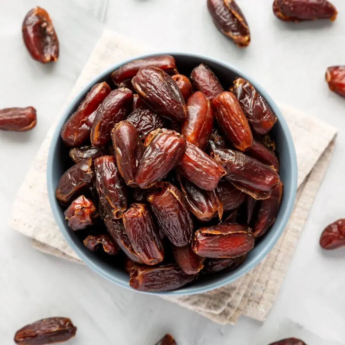 Bowl of fresh, sweet dates on a linen napkin, surrounded by more dates for a healthy snack.