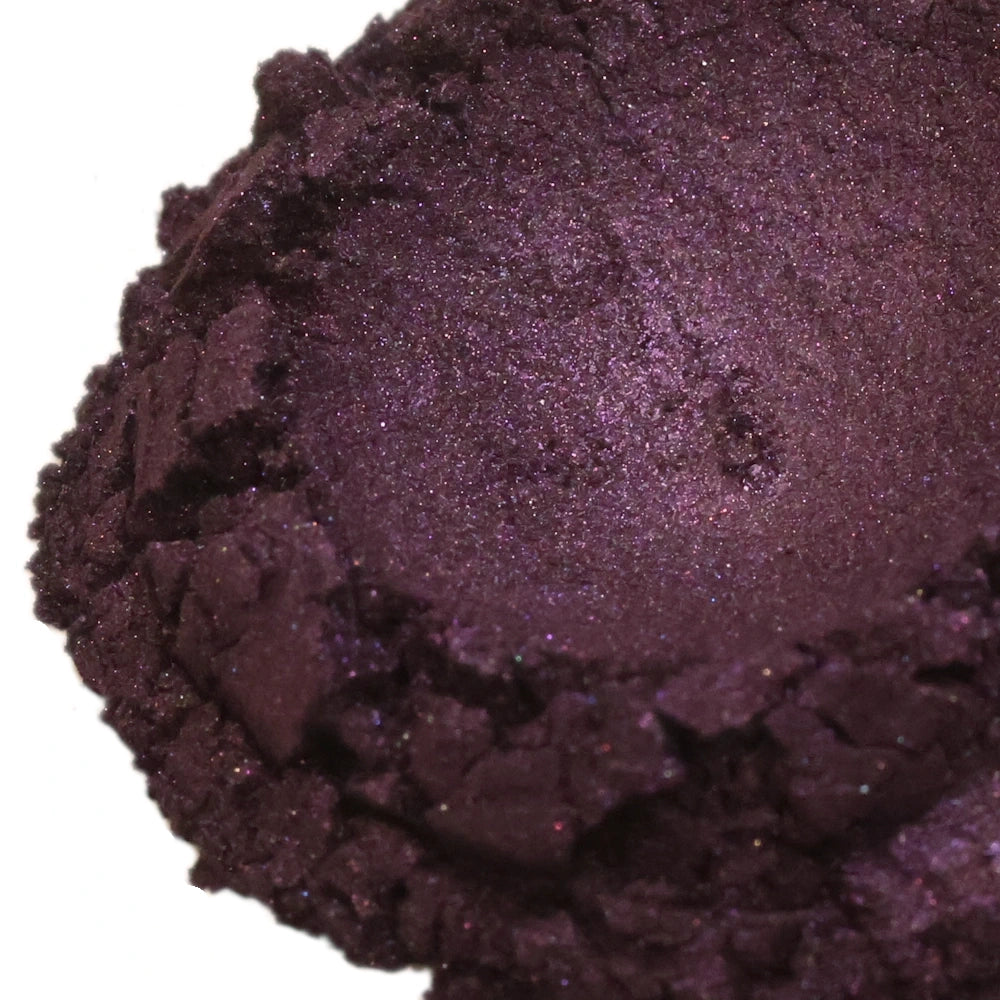 Close-up view of a deep purple loose powder with a shimmery, textured surface and cracked edges.