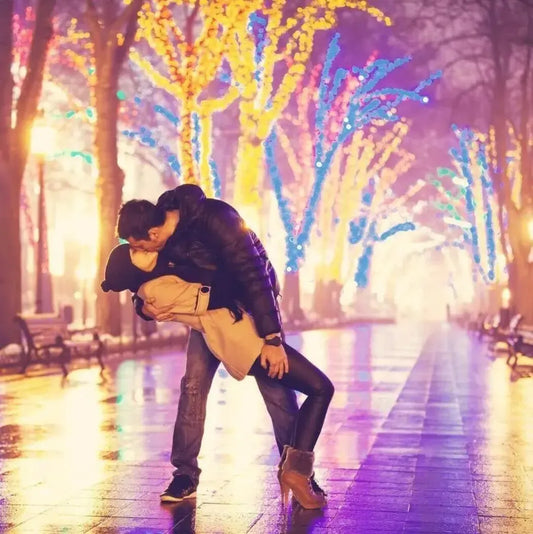Couple sharing a romantic kiss under colorful lights in a beautifully lit park.