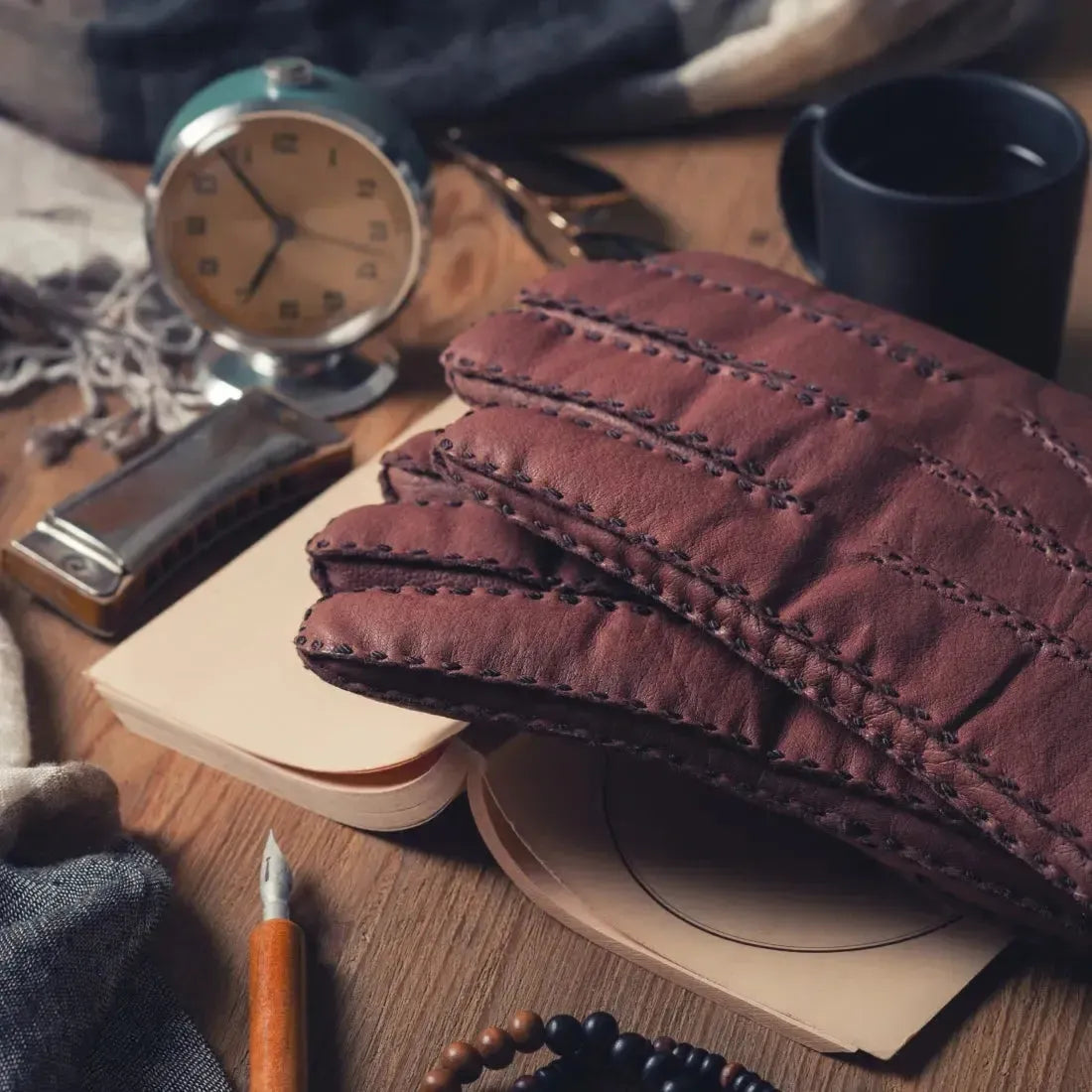 Luxurious brown leather gloves on a stylish wooden table with a clock and coffee cup.