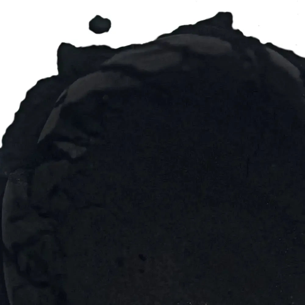 A close-up of Activated Charcoal Natural Pigment, a dark, powdery substance with uneven edges and a small clump above the main area, set on a white background.