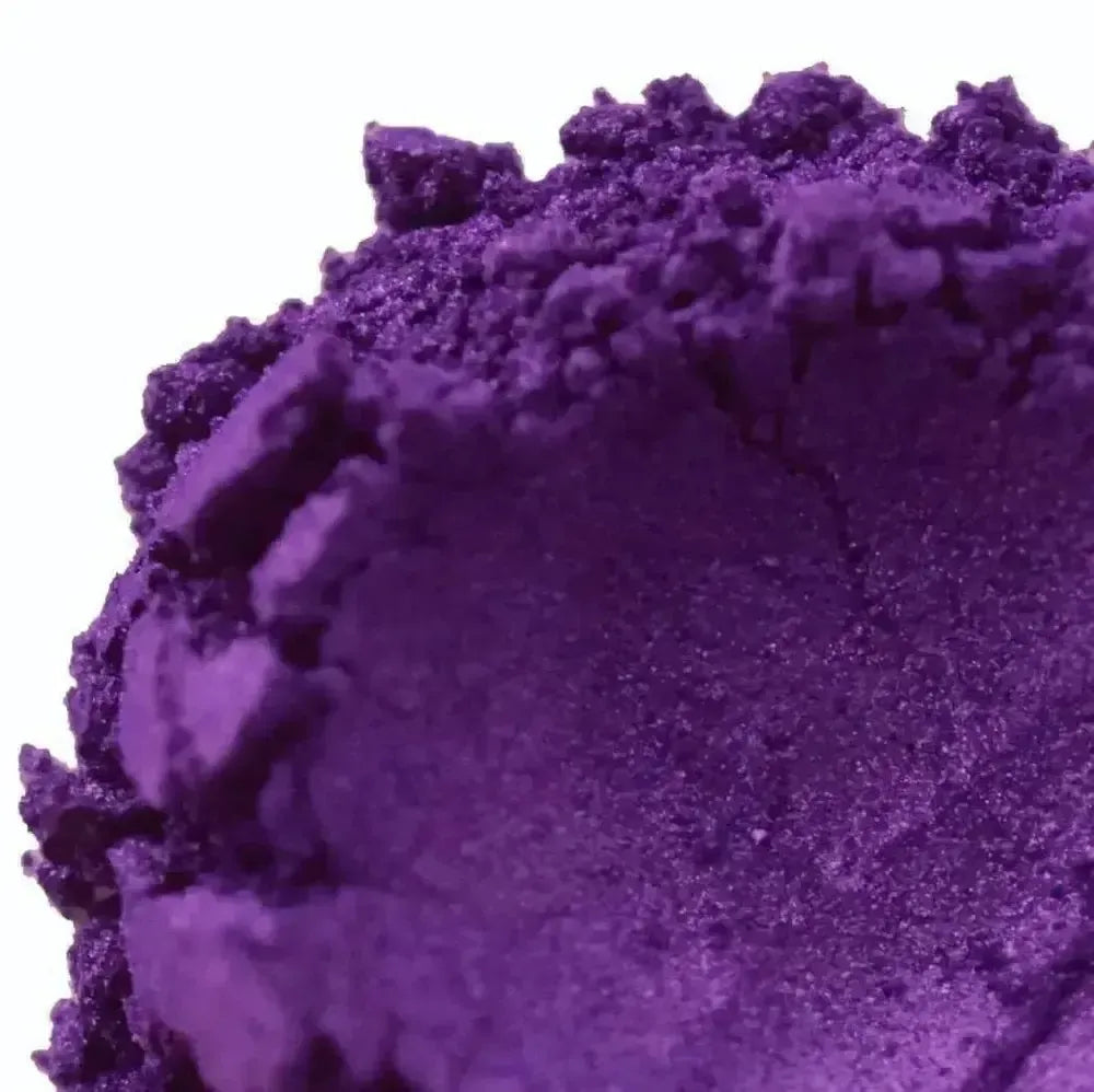 Close-up of Purple Vibrance Mica powder, crushed on a white background, showing its vibrant purple color, rough texture, and uneven edges.