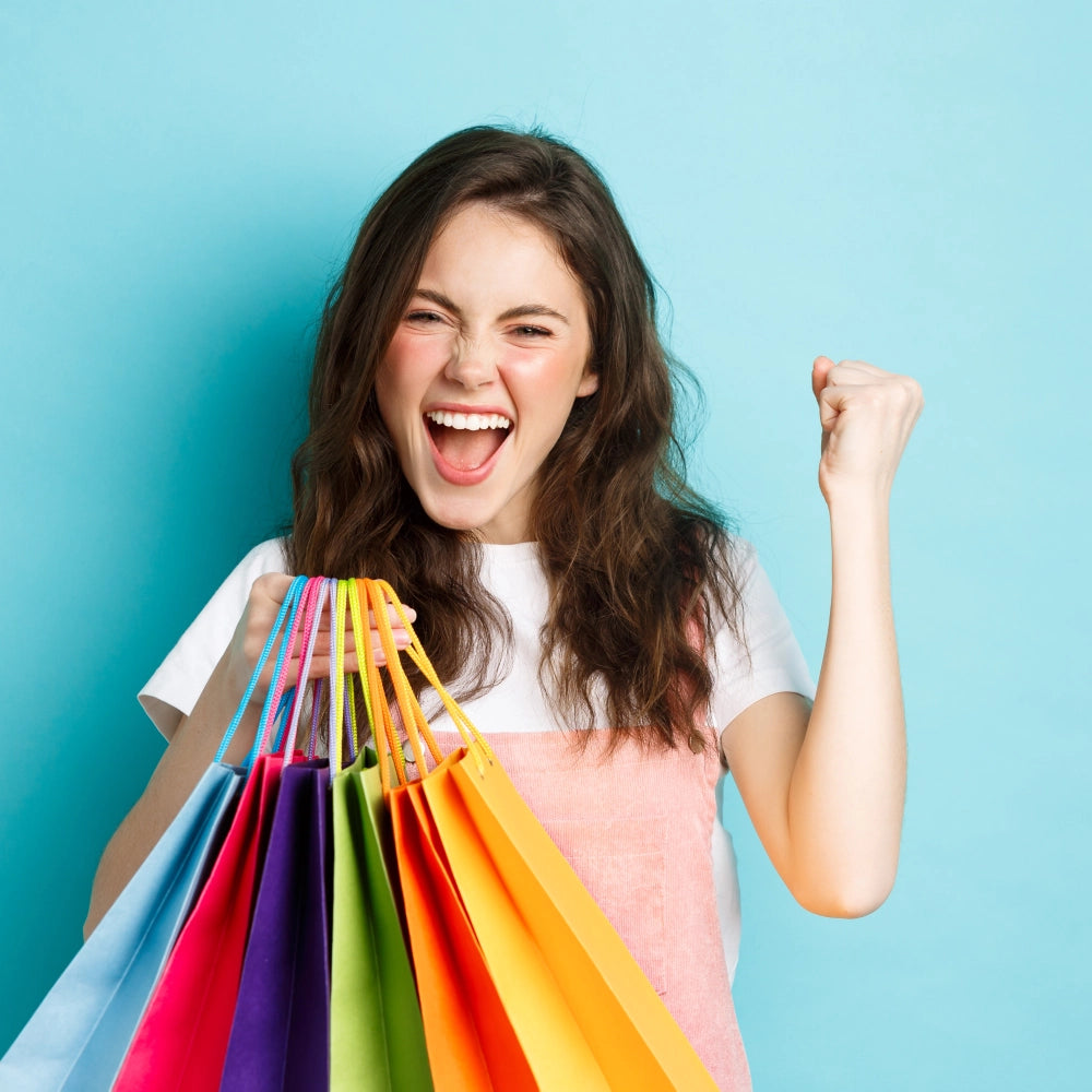 Joyful woman celebrating a successful shopping spree with colorful bags against a blue background.