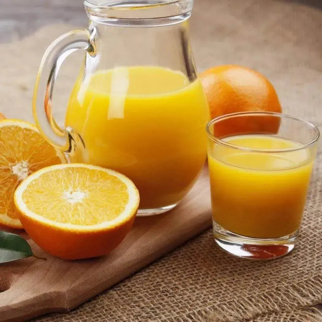 Clear glass pitcher of vibrant Satsuma orange juice with fresh oranges on wood