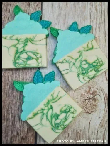 Three decorative soap bars resembling cupcakes with green swirls and blue frosting, resting on a wooden surface.