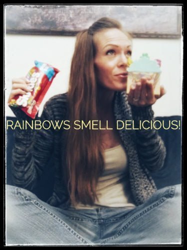 Woman holding a colorful cupcake and candy pack with "Rainbows Smell Delicious!" text.