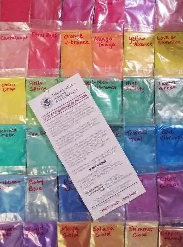 Colorful soap colorants arranged in bags with a notice of baggage inspection in the center.