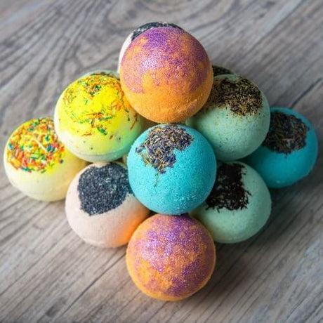 Colorful handmade bath bombs in a pyramid stack on a wooden surface.