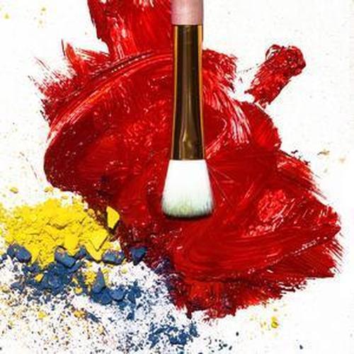 A makeup brush over vibrant red, yellow, and blue pigments, perfect for creating bold makeup looks.