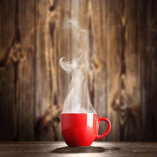 Steaming red coffee mug on rustic wooden table against wooden background.