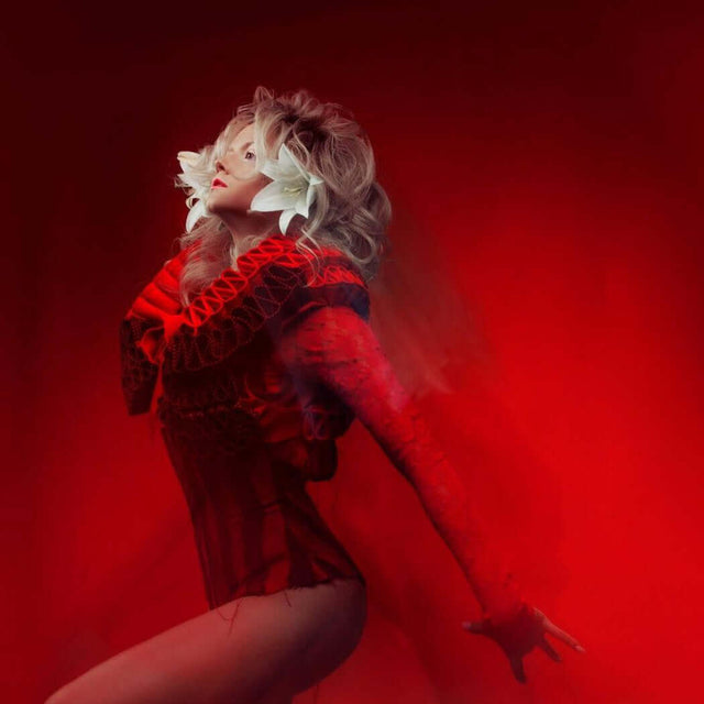 Woman in red elaborate outfit with white feathers, posing gracefully against a red background. Nurture Handmade fashion.