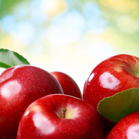 Fresh red apples with green leaves against a blurred green and yellow background.