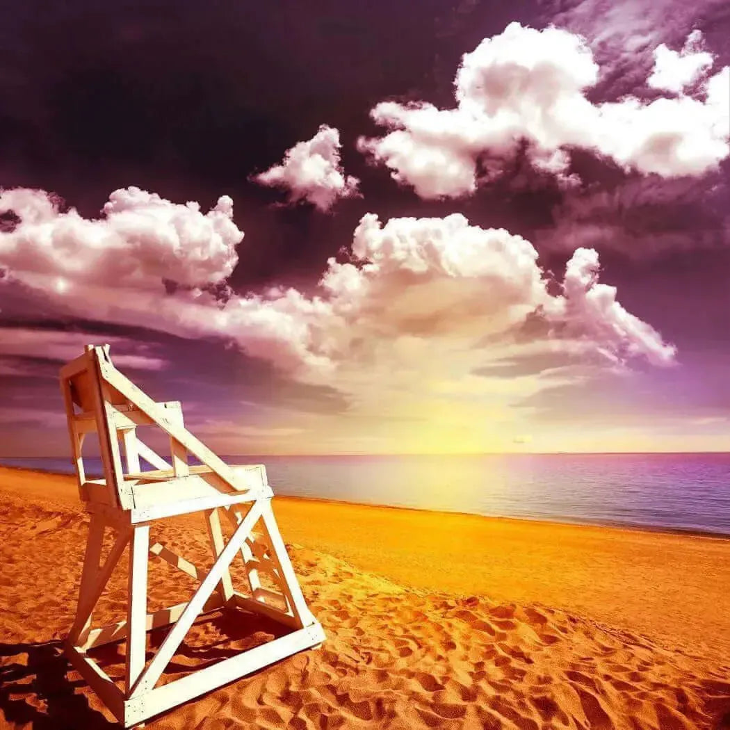 Scenic beach view with a lifeguard chair under a vibrant sunset and fluffy clouds.