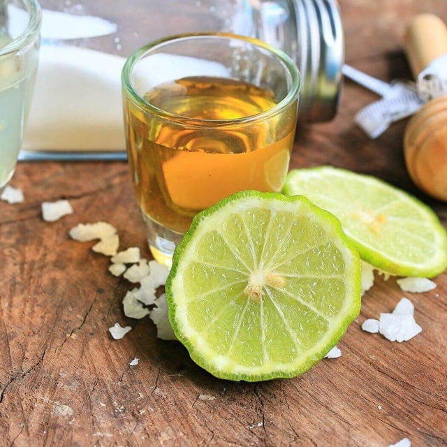 Fresh lime slices and a glass of golden liquid on wooden table, showcasing natural ingredients in nurture handmade products.