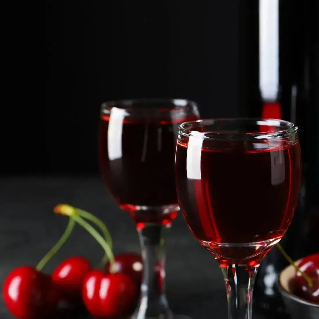 Two clear glass wine glasses with red Black Cherry Merlot fragrance oil and fresh cherries