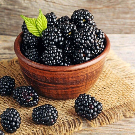 Fresh blackberries in a wooden bowl on a rustic background with burlap fabric, showcasing Nurture Handmade's natural produce.