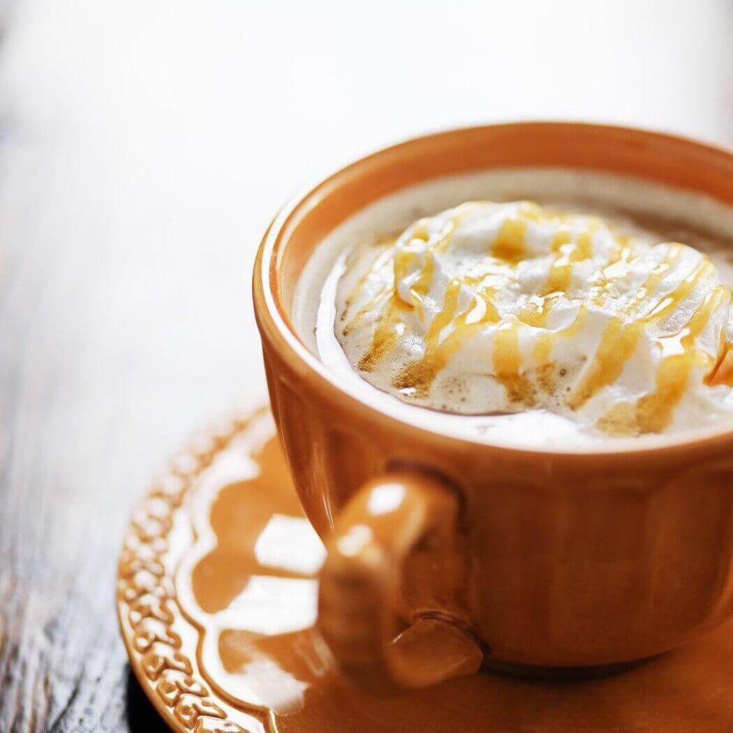 Caramel-topped latte in a handmade orange ceramic cup on a matching saucer.