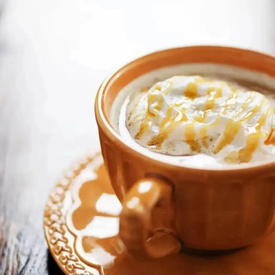 Orange ceramic cup of frothy coffee with caramel drizzle, saucer