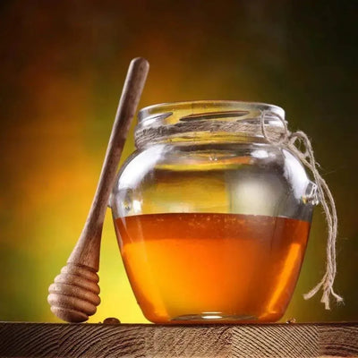 Glass jar of golden honey with twine and wooden dipper