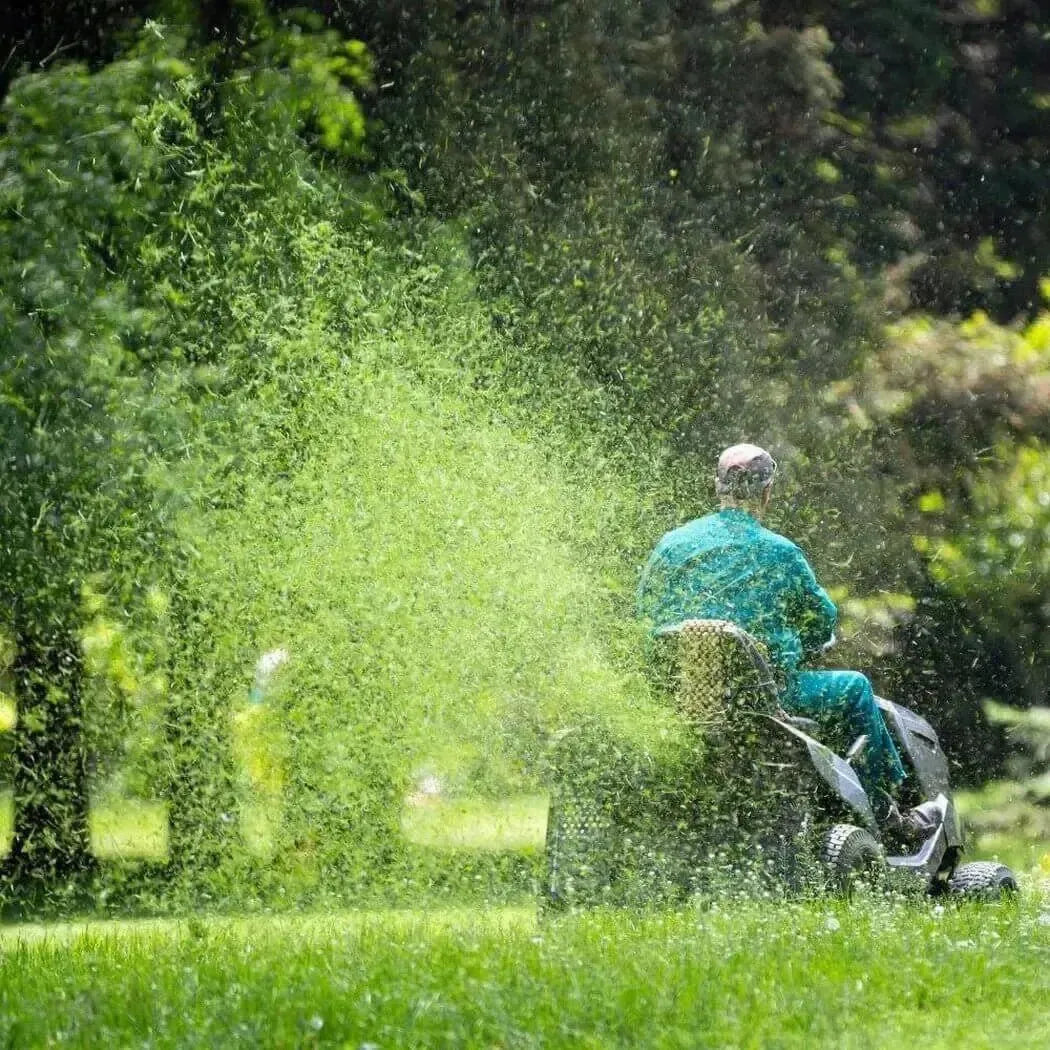 Person in teal outfit on black silver CLIBBINS mower spraying green grass clippings
