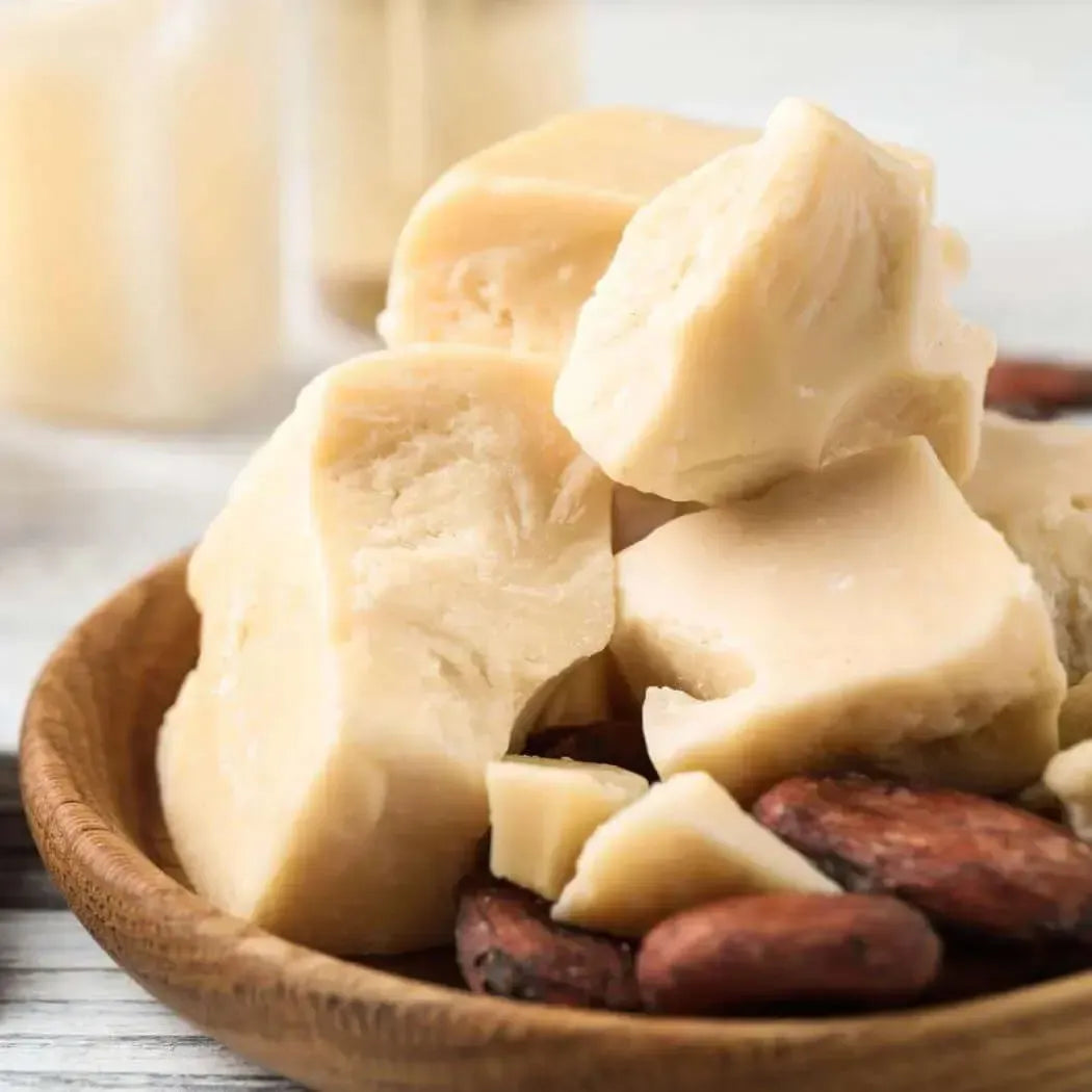Natural cocoa butter chunks nestled in a wooden bowl with cocoa beans, perfect for skincare and fragrance blends.