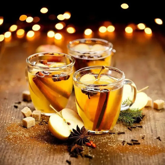 Festive warm apple cider with spices in clear mugs, surrounded by apples and sugar, twinkling holiday lights.