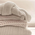 Stack of beige knitted blankets in Cuddlesome Fragrance Blend