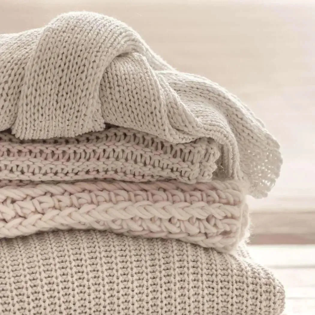 Stack of beige knitted blankets in Cuddlesome Fragrance Blend