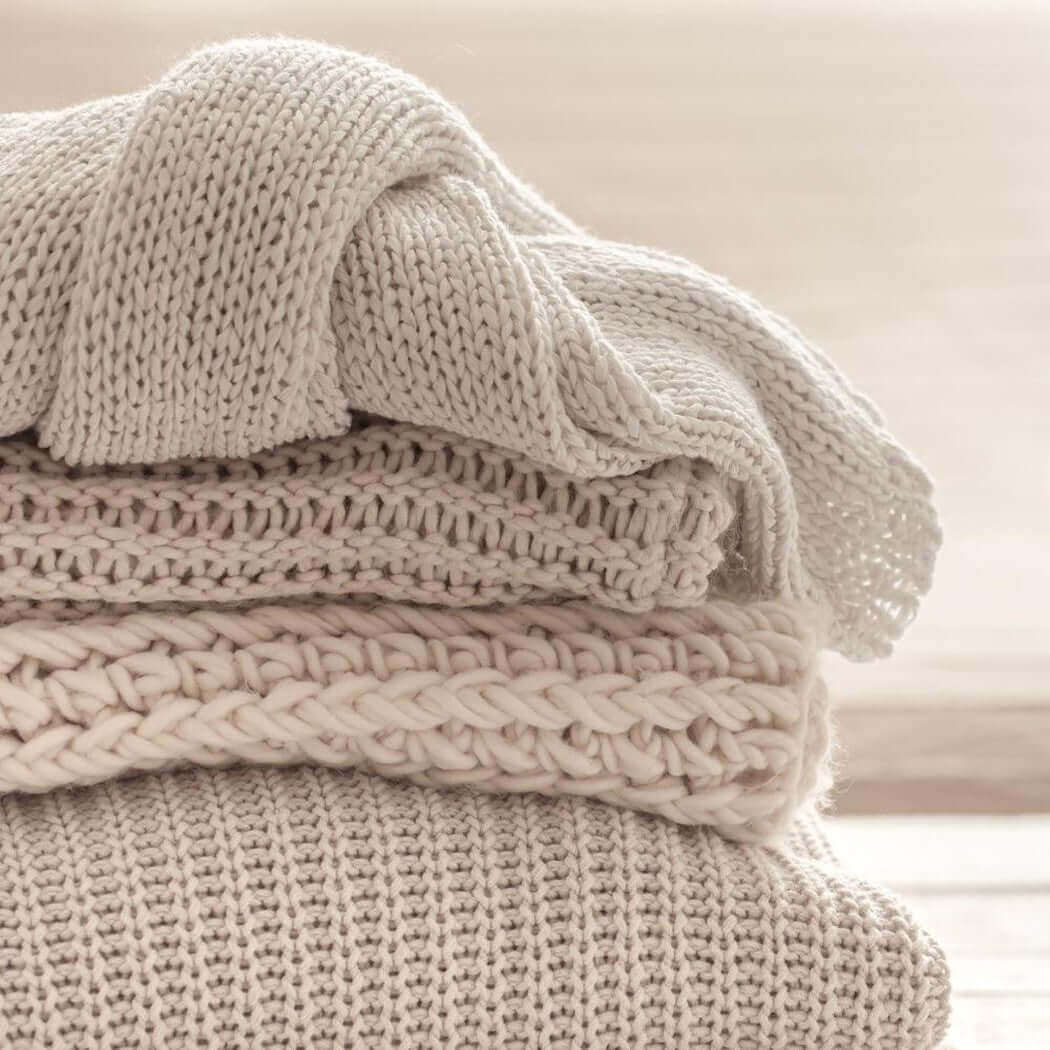 Soft, neutral-toned handmade knit blankets stacked neatly, showcasing intricate detailing perfect for nurturing cozy home decor.