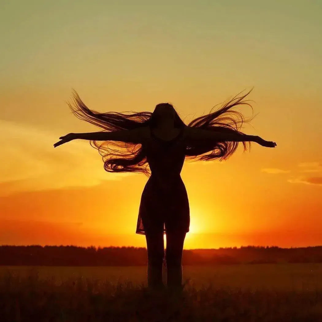 Silhouette of woman with flowing hair against orange sunset for Divinity Fragrance Blend