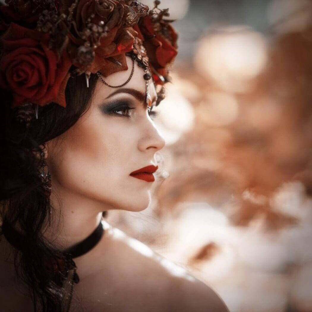 Profile of a woman with dramatic makeup wearing a flower crown and a choker, captured in a soft, dreamy light.