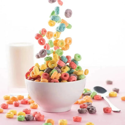 Colourful cereal rings falling into white bowl, milk glass behind