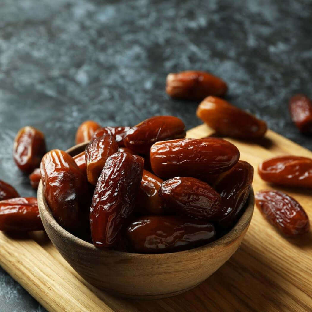 Wooden bowl filled with fresh dates on a cutting board, showcasing natural and nutritious dried fruits.