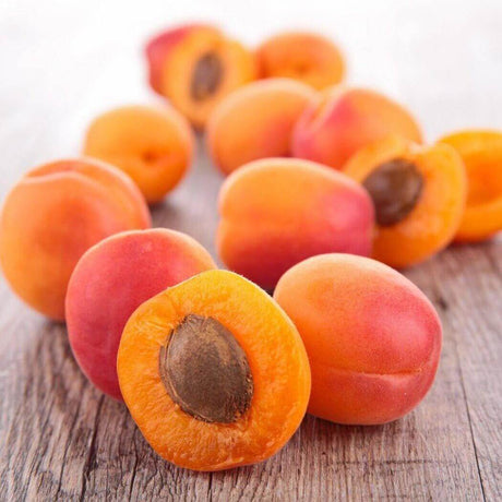 Fresh ripe apricots on a wooden surface, showcasing vibrant orange and red hues with seeds in the center.