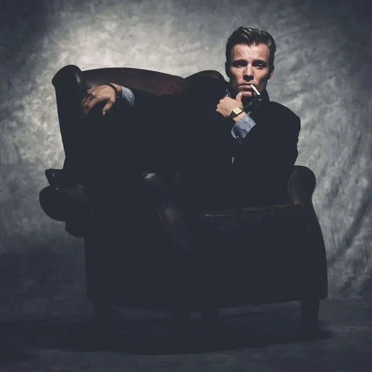 Sophisticated man in a dark suit lounging in an elegant armchair, embodying confidence and luxury.