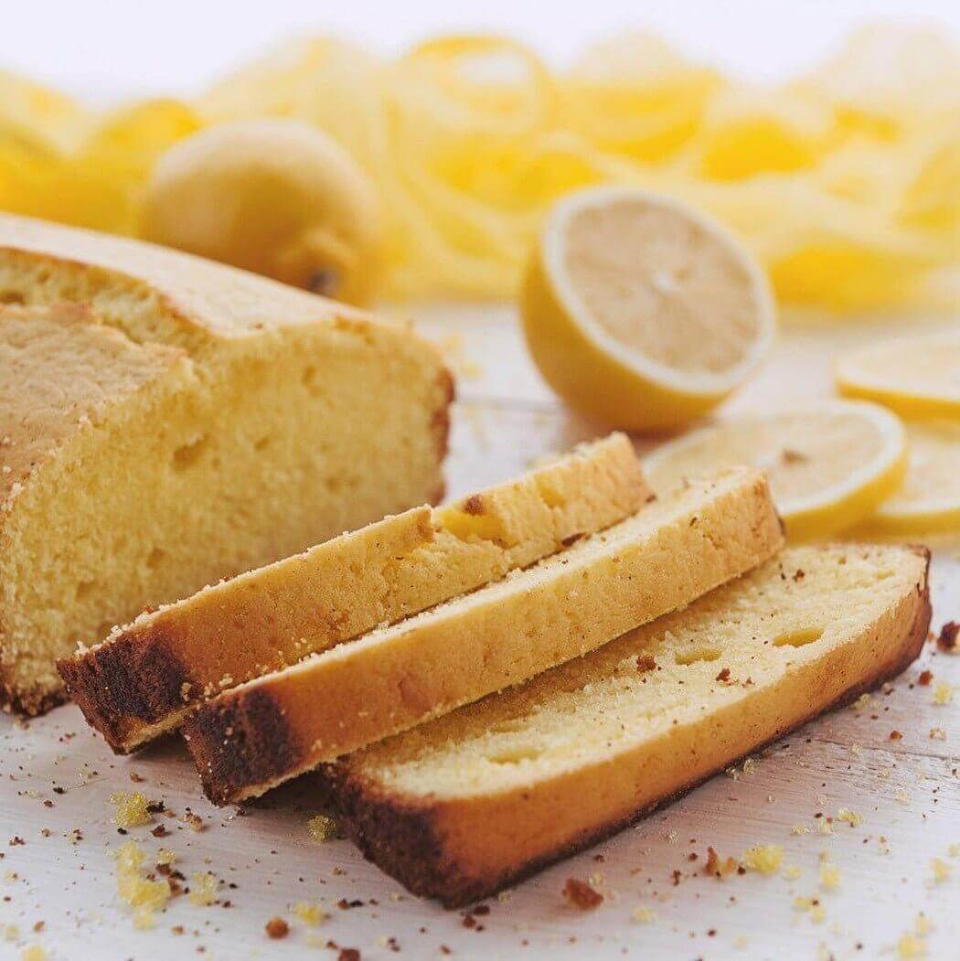 Freshly sliced homemade lemon bread on a wooden cutting board with whole and halved lemons in the background. Perfect for nurturing handmade treats.