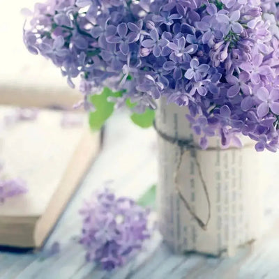 Purple lilac blooms in paper-wrapped jar beside open book