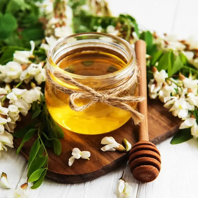 Glass jar of honey tied with twine, white blossoms around