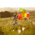 Child in floral dress runs through sunlit field with colorful balloons, Nirvana Fragrance Blend