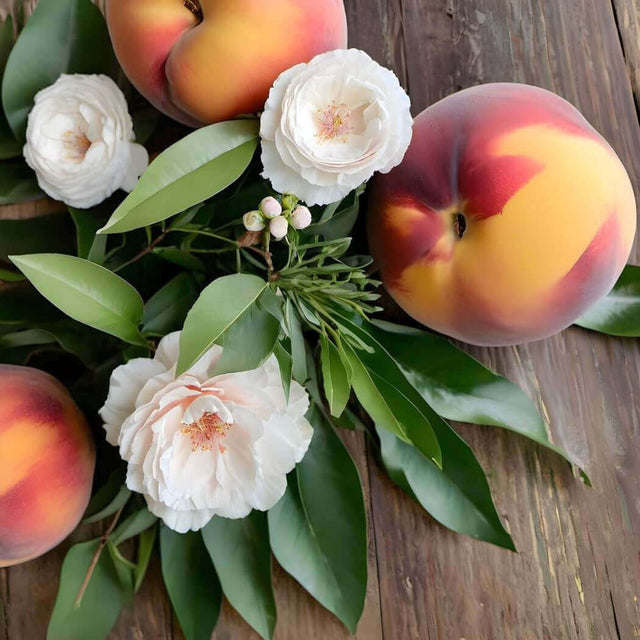 Fresh peaches and white flowers with green leaves on a rustic wooden surface from Nurture Handmade.