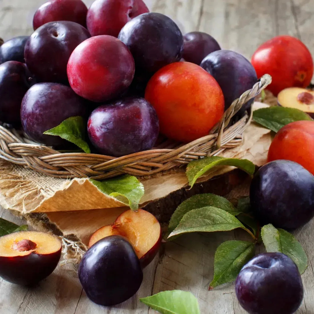 Fresh plums in a wicker basket with green leaves, showcasing rich colors and juicy texture for fragrance oil inspiration.