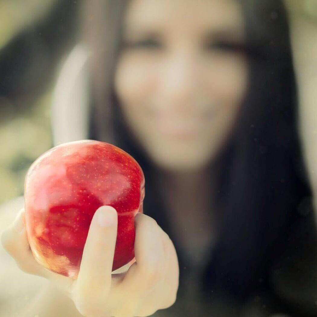 Woman holding a shiny red apple with blurred background