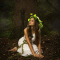 Woman in white dress with green leafy crown sits by tree for Reverie Fragrance Oil