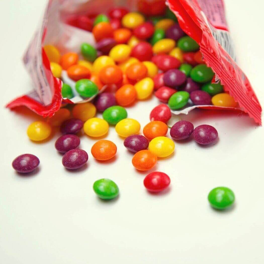 Colorful candy spilling from an open red packet on a white surface