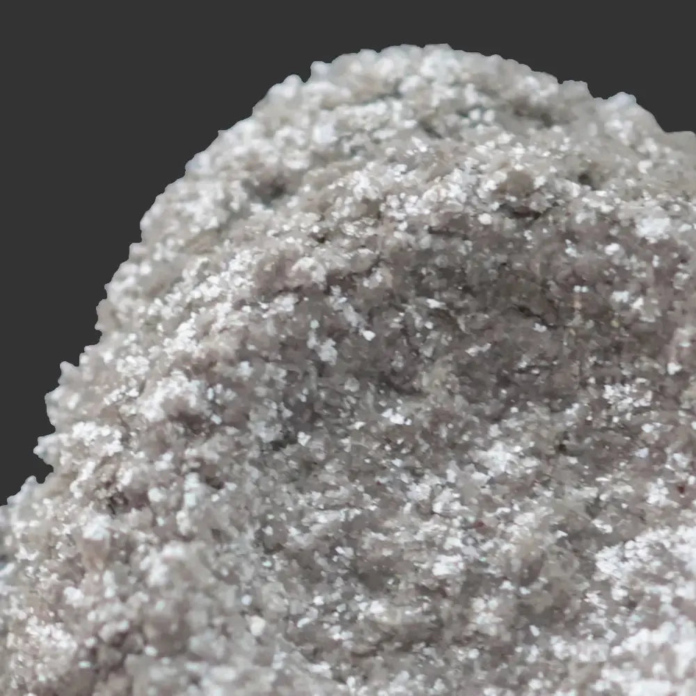 Close-up of Snowflake Sparkle White Mica’s rough, grayish surface with sparkling white crystals that create a diamond-like shimmer against a dark background.