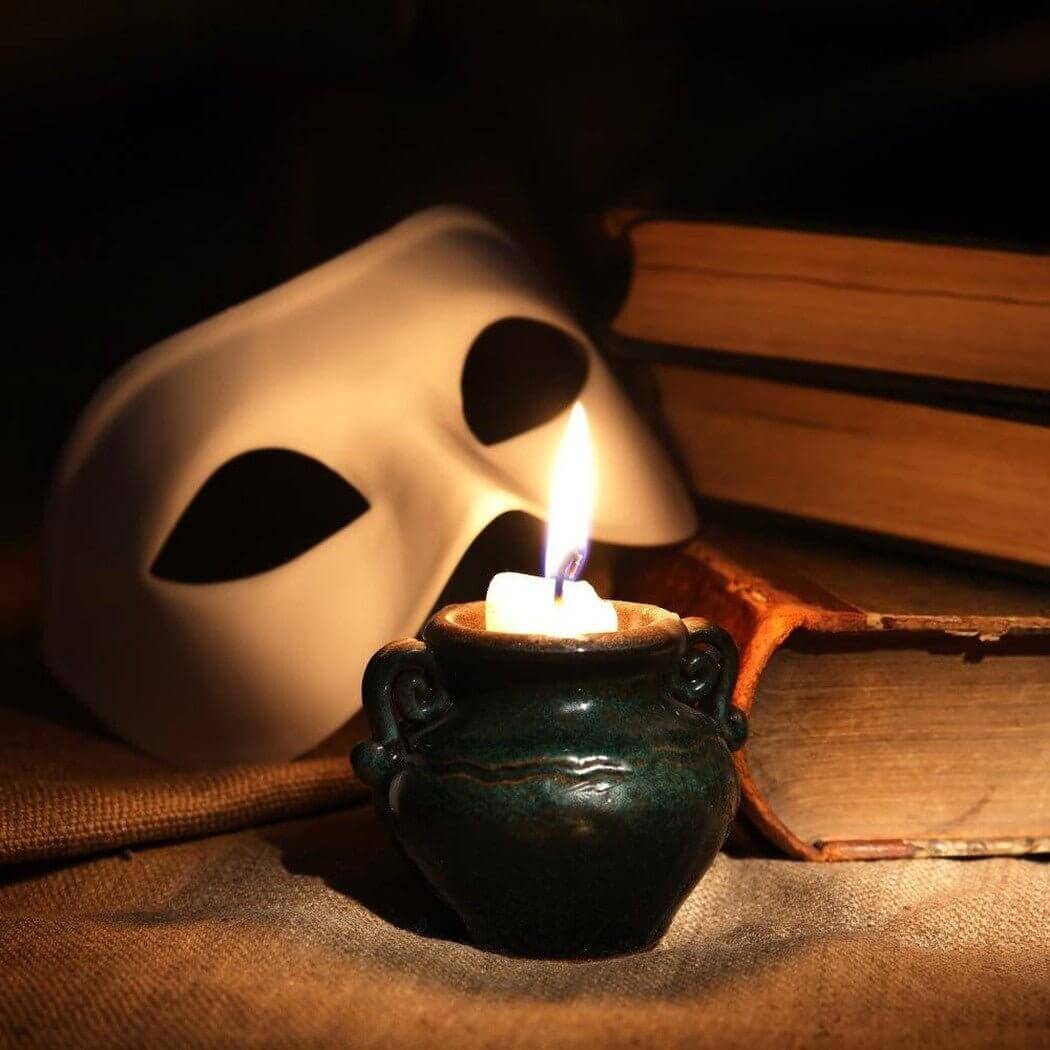 Handmade candle in dark vase with mask and old books, creating a cozy and mysterious ambiance. Nurture Handmade products.