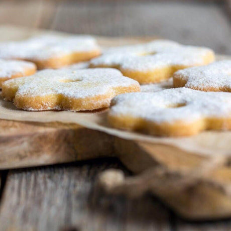 Homemade flower-shaped cookies dusted with powdered sugar on a wooden serving board. Nurture Handmade baking.