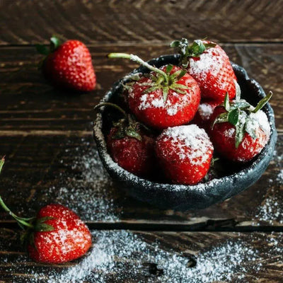 Black bowl of strawberries dusted with powdered sugar on dark wood